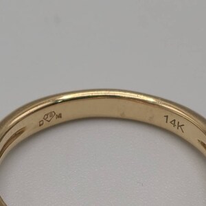 May include: Close-up of a gold ring with small diamonds set along the band. The ring is marked with "14K" and other markings. The ring is a jewelry item.