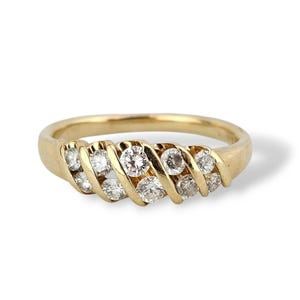 A gold ring with a series of clear, round-cut diamonds set in a diagonal pattern. The ring has a smooth, polished band and a classic, elegant design. The diamonds sparkle against the gold setting.