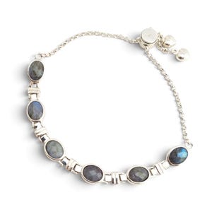 May include: A silver bracelet featuring six oval-shaped, faceted labradorite stones set in polished metal links. The bracelet includes a delicate chain section with an adjustable sliding clasp mechanism and two small heart-shaped charms at the end.