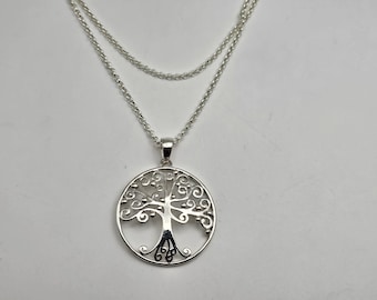 May include: A silver necklace with a delicate chain and a pendant in the shape of a tree of life. The pendant is circular and features a detailed design of a tree with branches and roots.