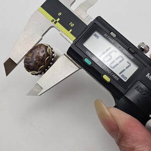 K&ouml;nnte beinhalten: Nahaufnahme eines Rings aus braunem und wei&szlig;em Achat mit einer silbernen Fassung. Der Ring wird mit einer digitalen Schieblehre gemessen, die 16,07 mm anzeigt.