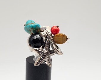 May include: A silver ring with a black onyx stone, turquoise, tiger's eye, and red coral beads. The ring has a dangling starfish charm.