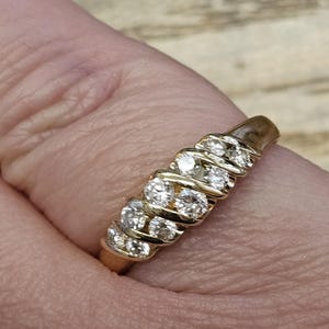 Puede incluir: Un anillo de oro con una serie de piedras preciosas redondas y claras. El anillo est&aacute; en un dedo, y la banda de oro tiene una apariencia texturizada. Las piedras preciosas est&aacute;n espaciadas uniformemente y captan la luz.