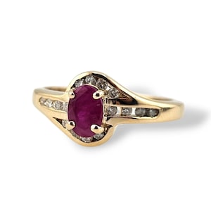 May include: A gold ring featuring a large oval ruby center stone. The ring is accented with small diamonds and has a classic, elegant design. The band is a polished gold color.