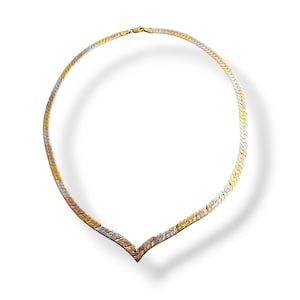 May include: A tri-color necklace with a herringbone design. The necklace features gold, rose gold, and silver tones. The necklace is a choker style and has a V-shaped pendant. The clasp is gold.