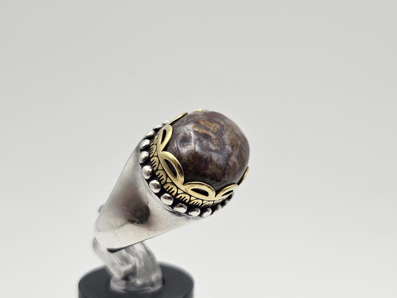 K&ouml;nnte beinhalten: Ein silberner Ring mit einem braunen und goldenen Stein. Der Stein ist in einer goldenen Fassung gefasst und der Ring ist mit einem goldenen Band verziert.