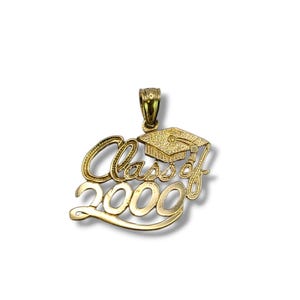 May include: A gold-colored pendant with the words "Class of 2000" in a cursive font, topped with a graduation cap. The pendant is designed to be worn as a necklace.