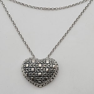 May include: A silver chain necklace with a heart-shaped pendant. The pendant is intricately designed with a woven pattern.