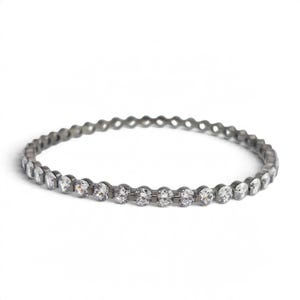 May include: A thin, circular eternity band crafted from dark, gunmetal-toned metal. The ring features a continuous row of small, round, clear, faceted stones set closely together, creating a sparkling, uniform appearance around the entire band.