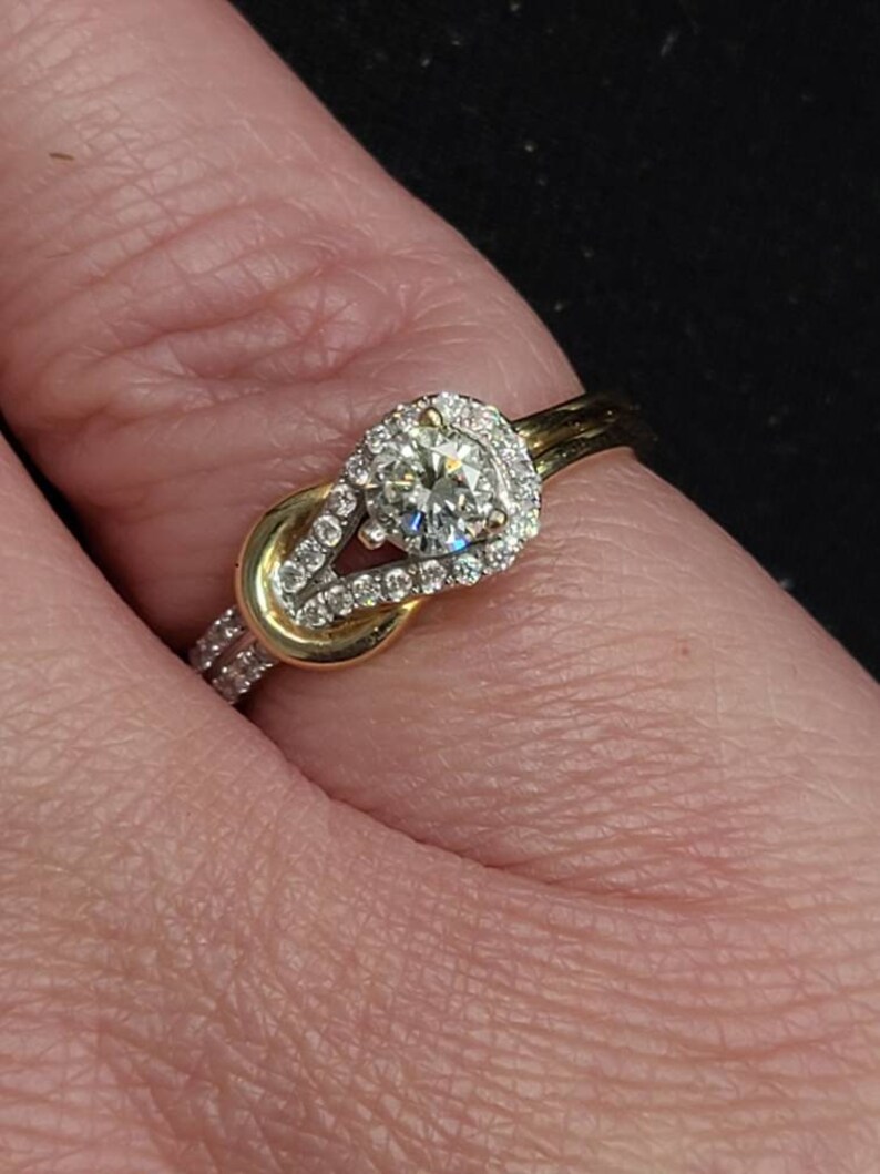 May include: A gold and diamond ring with a knot design. The ring features a large, round, clear diamond surrounded by smaller diamonds. The band is gold with additional small diamonds.