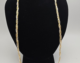 Könnte beinhalten: Eine goldene und silberne Kettenkette mit einem gedrehten Design. Die Kette wird auf einer schwarzen Schaufensterpuppe präsentiert.