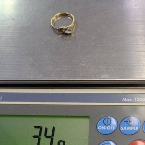 May include: A gold ring with a central diamond and smaller accent stones. The ring is on a digital scale, which reads 3.4 grams. The ring has a classic design.