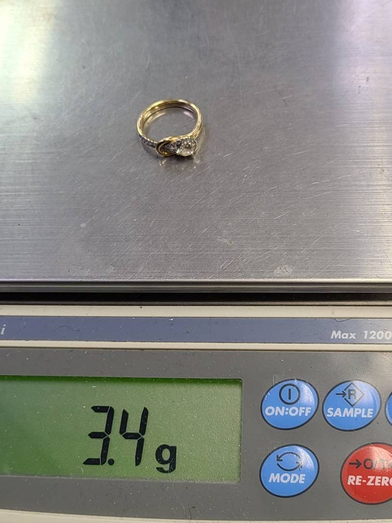 May include: A gold ring with a central diamond and smaller accent stones. The ring is on a digital scale, which reads 3.4 grams. The ring has a classic design.