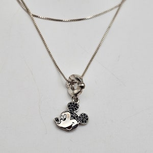 May include: A silver necklace with a Mickey Mouse pendant. The pendant features a detailed Mickey Mouse head with black gem accents. The necklace has a delicate chain design, perfect for everyday wear.