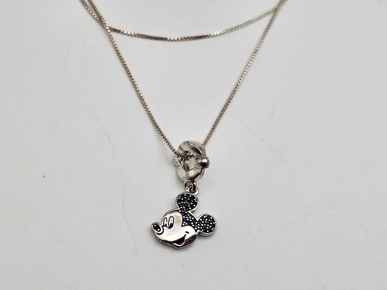 May include: A silver necklace with a Mickey Mouse pendant. The pendant features a detailed Mickey Mouse head with black gem accents. The necklace has a delicate chain design, perfect for everyday wear.