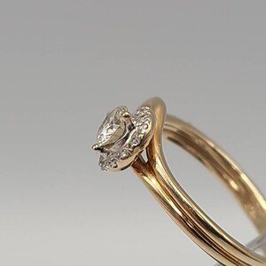 May include: A gold ring featuring a pear-shaped diamond center stone surrounded by a halo of smaller diamonds. The band is a smooth, polished gold. The ring is set against a neutral background.