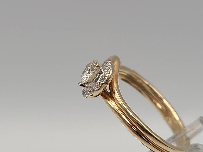 May include: A gold ring featuring a pear-shaped diamond center stone surrounded by a halo of smaller diamonds. The band is a smooth, polished gold. The ring is set against a neutral background.