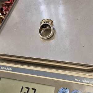 K&ouml;nnte beinhalten: Ein silberner Ring mit einem schwarzen Stein und goldenen Akzenten. Der Ring liegt auf einer digitalen Waage, die 13,7 g anzeigt.