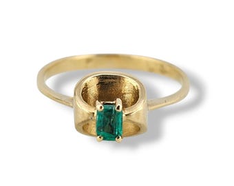 May include: A gold ring featuring a rectangular, emerald-cut green gemstone. The ring has a unique design with a thick band and a bezel setting that holds the gemstone securely. The ring is displayed against a white background.
