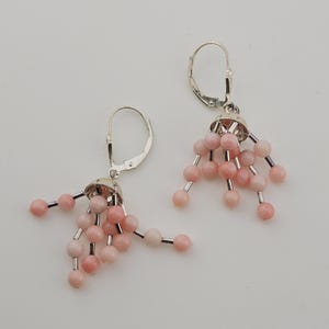 May include: A pair of silver-tone earrings with a cluster of pink beads. Each earring features a silver cap with multiple strands of pink beads, creating a dangling effect. The earrings have a lever-back closure.