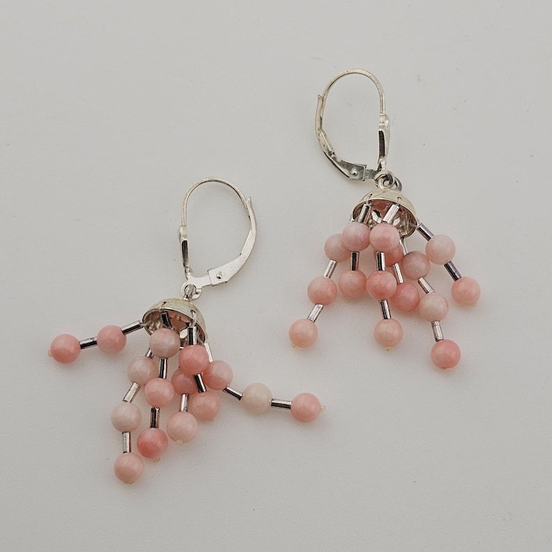 May include: A pair of silver-tone earrings with a cluster of pink beads. Each earring features a silver cap with multiple strands of pink beads, creating a dangling effect. The earrings have a lever-back closure.