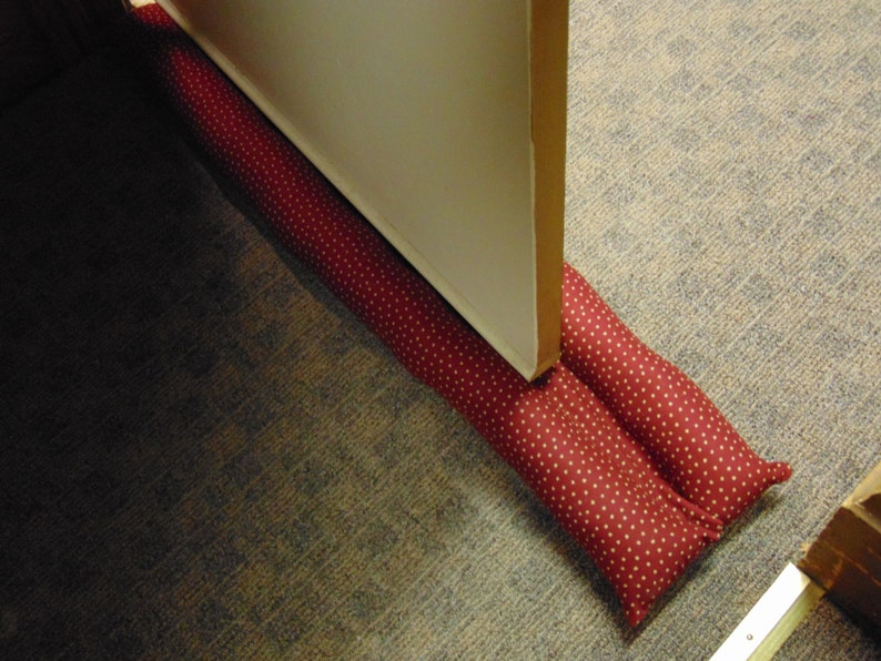 May include: A red doorstop with white polka dots is placed under a closed white door. The doorstop is made of fabric and is filled with padding.