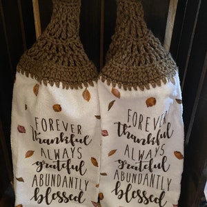 May include: Two brown crocheted kitchen towels with white fabric and the text "Forever thankful always grateful abundantly blessed" on each towel.