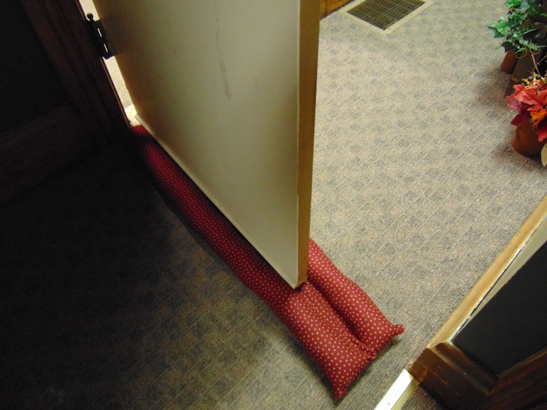 May include: Red and white polka dot doorstop made of fabric. The doorstop is placed under a closed door.