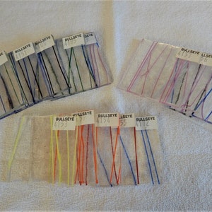May include: Close-up of eight glass samples with different colored glass stringers. The samples are labeled with the brand "Bullseye" and a number. The numbers are 4132, 4151, 4185, 4157, 4153, 4154, 4155, and 4112.