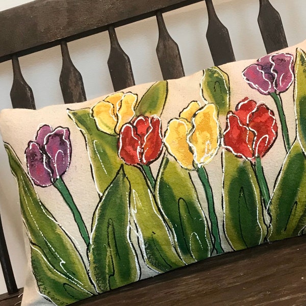 May include: A decorative pillow with a beige background featuring a floral design of yellow, red, and purple tulips with green leaves.