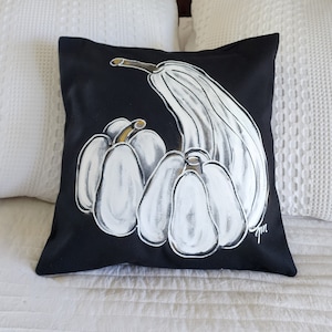 May include: Black pillow with a white hand-painted design of gourds. The gourds are arranged in a cluster with one long gourd curving around the others. The pillow has a white "gm" signature in the bottom right corner.