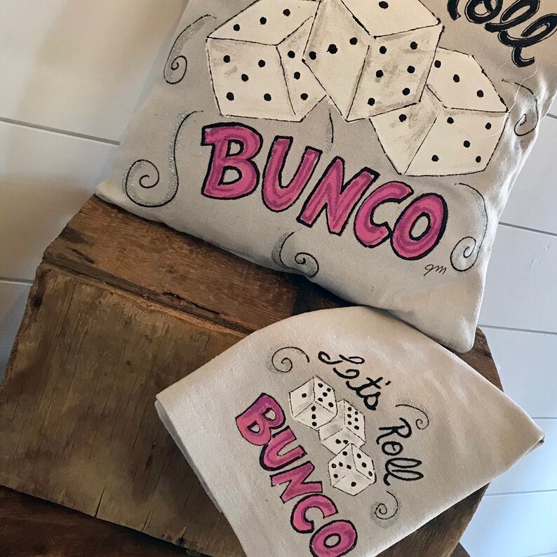 Peut inclure: Un coussin gris clair et une serviette carr&eacute;e assortie avec un motif de d&eacute;s et de texte. Le mot "Bunco" est en rose, et l'expression "Let's Roll" est en noir. Les d&eacute;s sont blancs avec des points noirs.