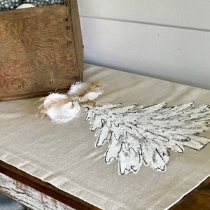 May include: A white linen table runner with a black and white painted leaf design and a burlap bow.