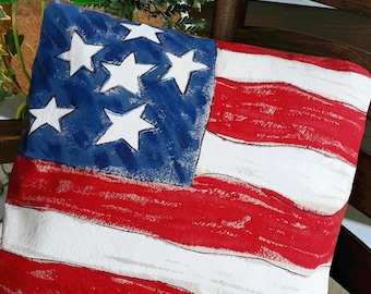 Peut inclure: Un coussin rouge, blanc et bleu avec un motif de drapeau américain peint. Le coussin est sur une chaise en bois.