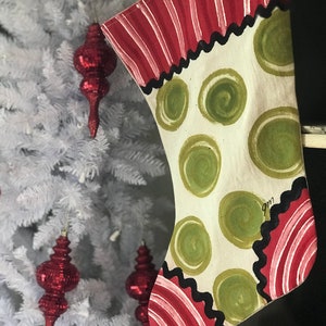 May include: A Christmas stocking with a white background and green polka dots. The stocking has a red and white striped cuff with a black trim.