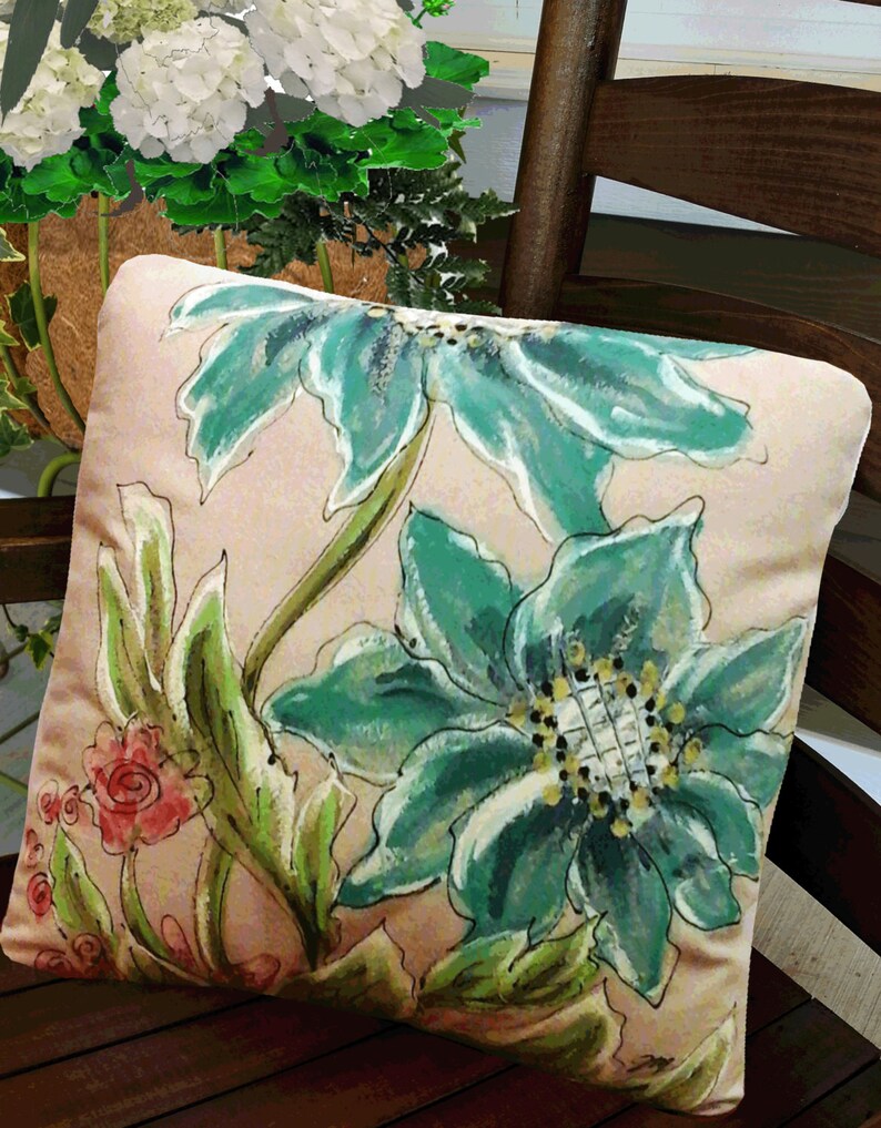 K&ouml;nnte beinhalten: Ein dekoratives Kissen mit einem Blumendesign mit gro&szlig;en, blaugr&uuml;nen Bl&uuml;ten und gr&uuml;nen Bl&auml;ttern auf einem hellrosa Hintergrund.