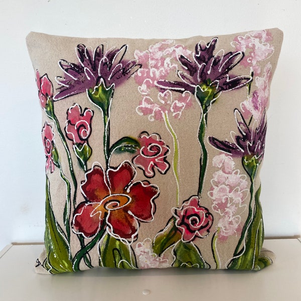 May include: A beige linen pillow with a floral design. The flowers are painted in shades of purple, pink, red, and green.