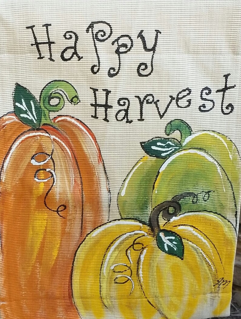 May include: A hand-painted burlap banner with the text "Happy Harvest" and three pumpkins. The pumpkins are painted in shades of orange, yellow, and green.