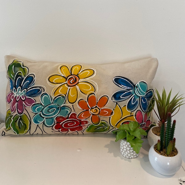May include: A decorative pillow with a beige background and a colorful floral design. The flowers are painted in shades of blue, yellow, red, green, and orange. 