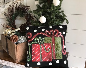 May include: A black and white polka dot cushion with a hand-painted design of red and green wrapped presents with a red ribbon and bow.