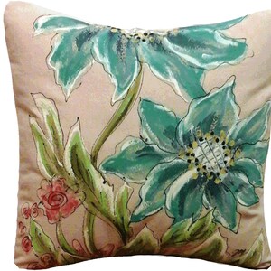 K&ouml;nnte beinhalten: Ein Dekokissen mit Blumenmuster. Das Kissen hat einen hellrosa Hintergrund mit gr&uuml;nen Bl&auml;ttern und zwei gro&szlig;en t&uuml;rkisblauen Blumen.