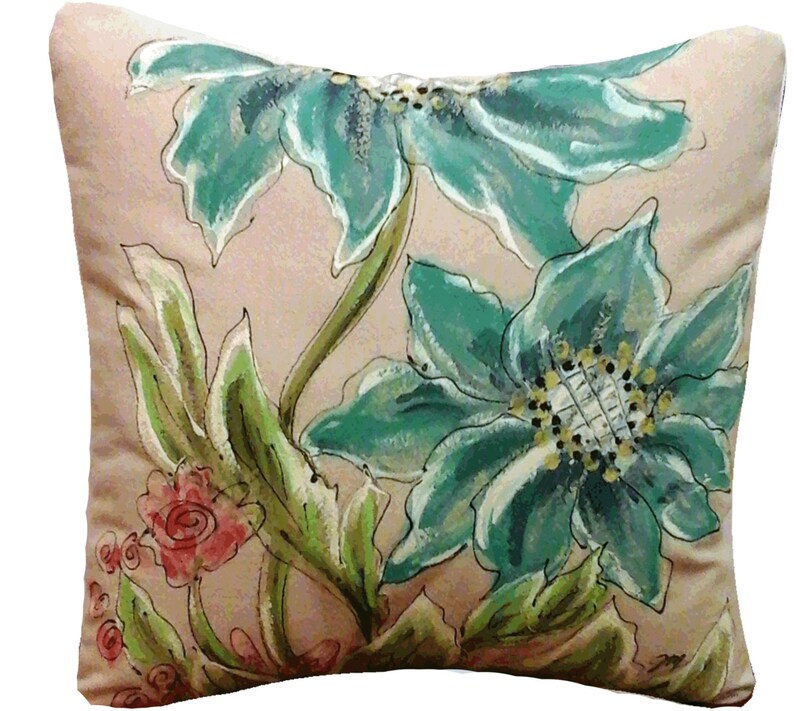 K&ouml;nnte beinhalten: Ein Dekokissen mit Blumenmuster. Das Kissen hat einen hellrosa Hintergrund mit gr&uuml;nen Bl&auml;ttern und zwei gro&szlig;en t&uuml;rkisblauen Blumen.