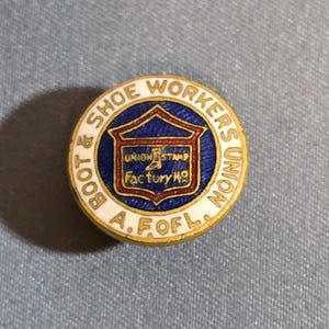 May include: A round, vintage pin with a gold border and the text "BOOT & SHOE WORKERS UNION A.F. OF L." The center features a blue and red design with the words "UNION STAMP Factory No."