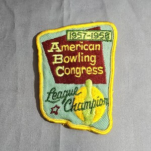 May include: A blue and yellow embroidered patch with the text "American Bowling Congress 1957-1958 League Champion" and a bowling pin graphic.