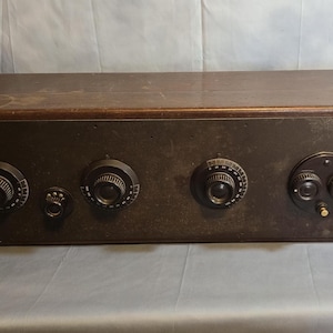 May include: A vintage wooden radio with five knobs and a brown finish. The radio has a rectangular shape and is sitting on a gray surface.