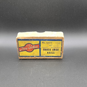May include: A vintage box of "True Value" brand horse shoe nails. The box is rectangular with a yellow and blue design and red text. The box is labeled "No. A471" and "1 lb."