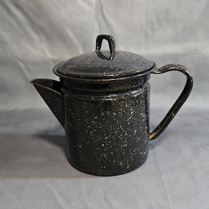 May include: Black and white speckled enamelware coffee pot with a lid and handle. The spout is on the left side. The handle is curved and attached to the side of the pot. The lid has a small handle on top.