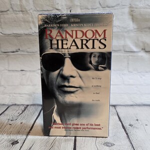 May include: A sealed VHS tape of the movie "Random Hearts" featuring Harrison Ford and Kristin Scott Thomas. The cover art shows Ford wearing sunglasses. Text includes the movie title and a quote from The New York Times.