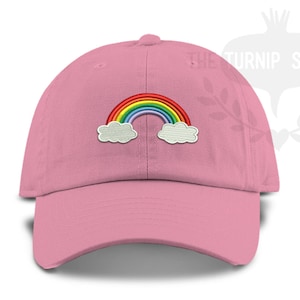 May include: A pink baseball cap with an embroidered rainbow and clouds. The rainbow is red, orange, yellow, green, blue, indigo, and violet. The clouds are white.
