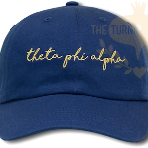 May include: A navy blue baseball cap with the text "theta phi alpha" embroidered in gold on the front.